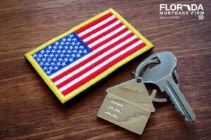 A fabric patch of the American flag placed beside a silver house-shaped keychain with a key, symbolizing homeownership and patriotism. The logo of Florida Mortgage Firm is displayed in the top right corner.